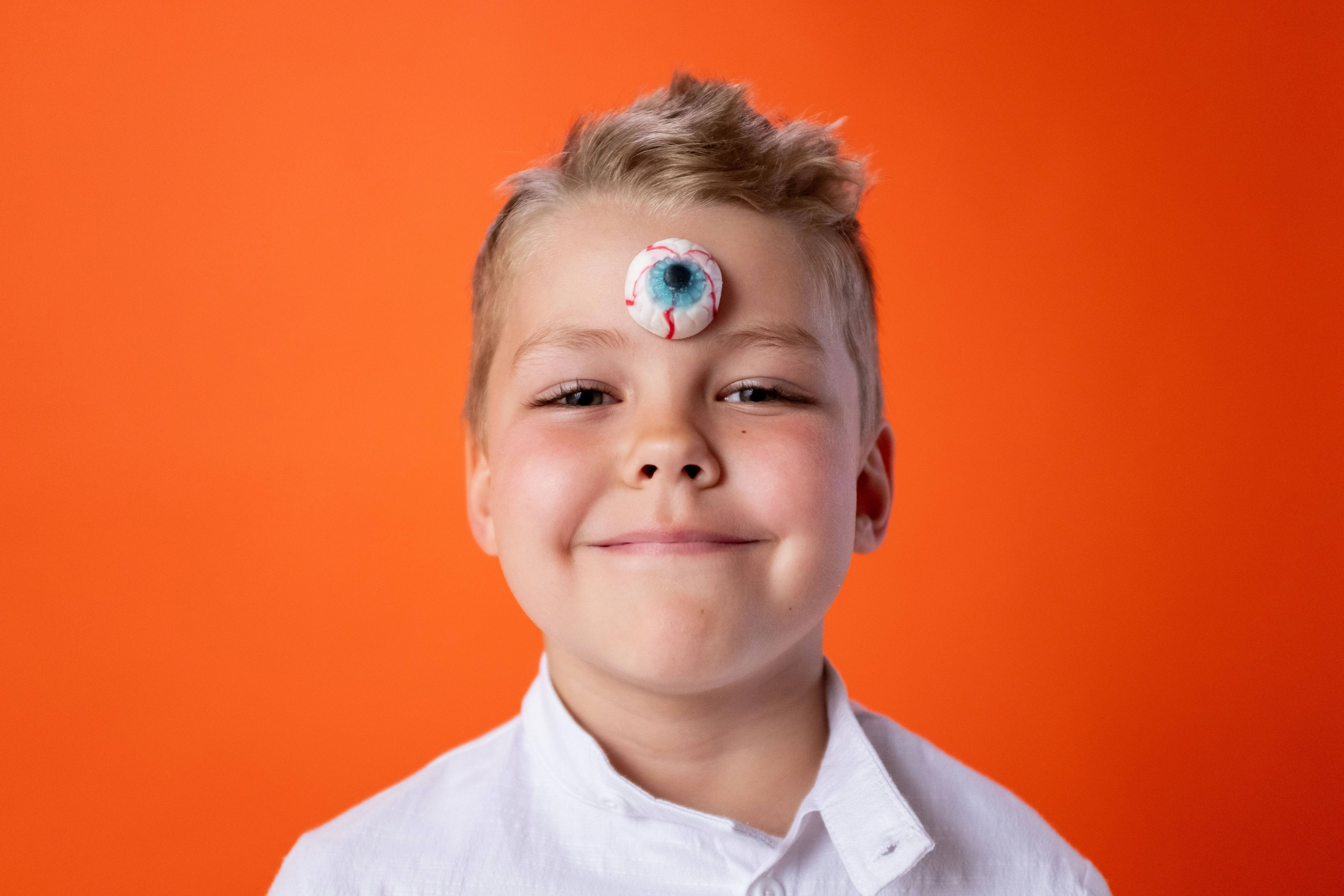 Boy with a candy shaped like an eye stuck on his forehead at the third-eye position – symbolic depiction of how artificial sweets cover inner perception and dull mental clarity