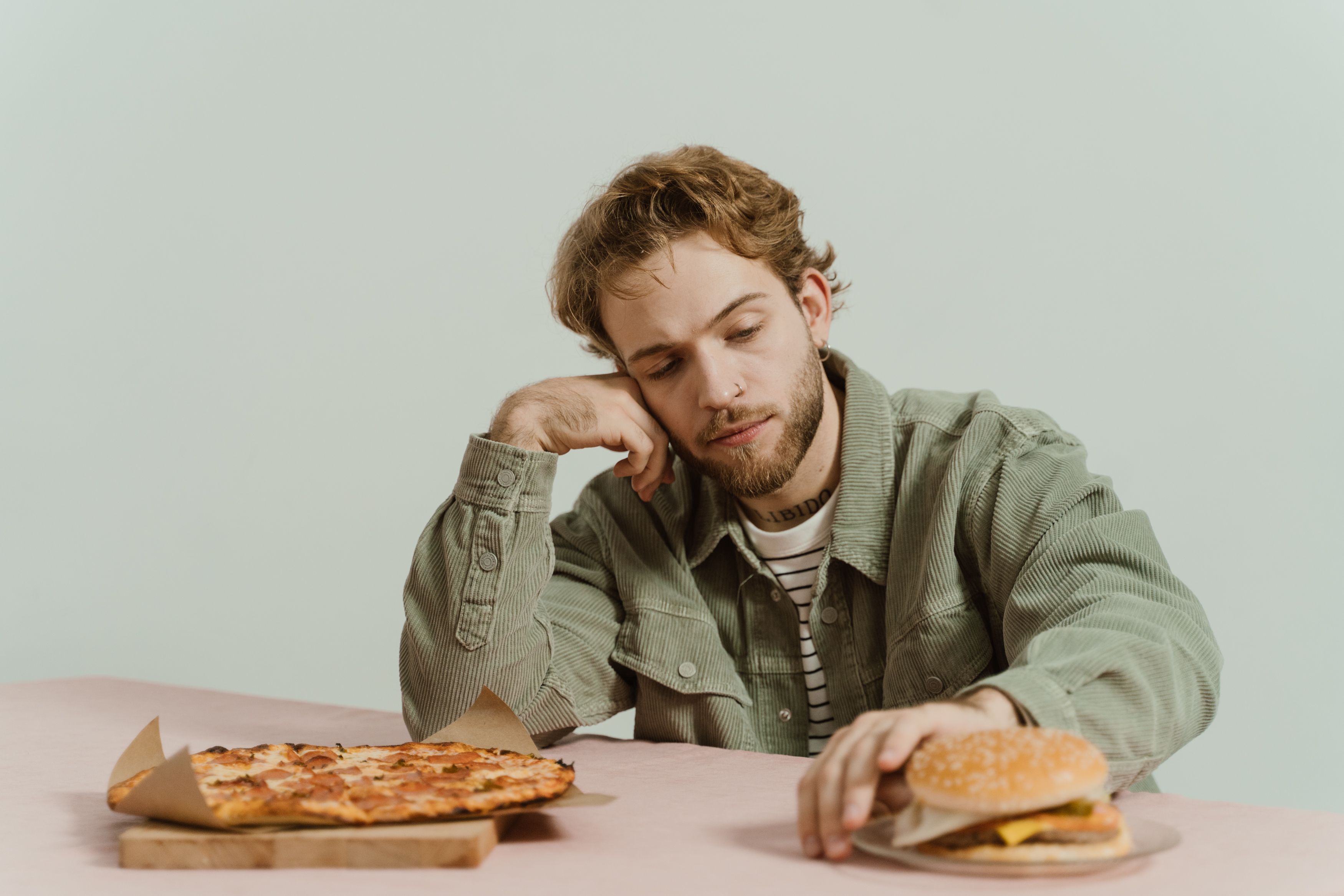 Man pushing away pizza and a hamburger with his hands – a conscious decision to limit inflammatory foods to support the gut and digestion.