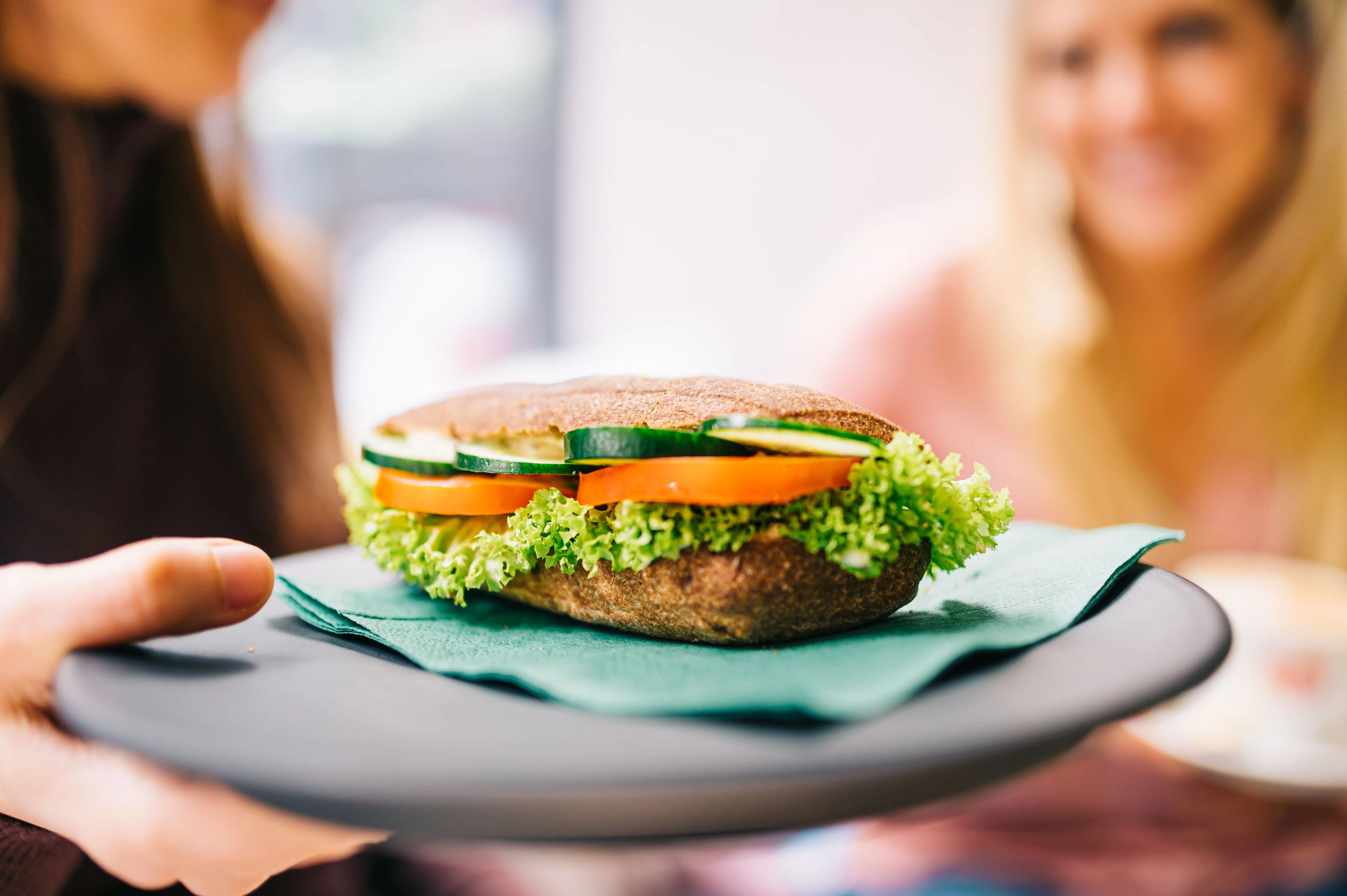 Woman offering a freshly topped healthy baguette on a plate – symbol of a conscious choice of real food instead of ultra-processed products